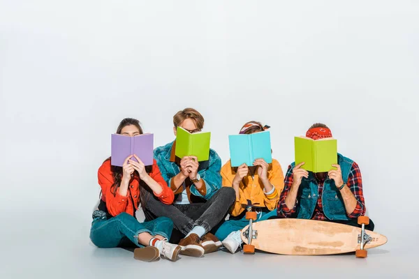 Jóvenes estudiantes sentados con monopatín y sosteniendo libros juntos - foto de stock