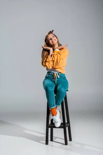 Attractive cheerful girl posing on stool on grey — Stock Photo
