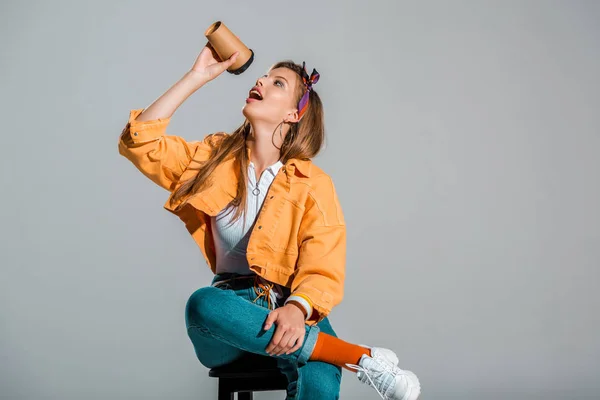 Приваблива стильна дівчина п'є каву, щоб піти ізольовано на сірому — стокове фото