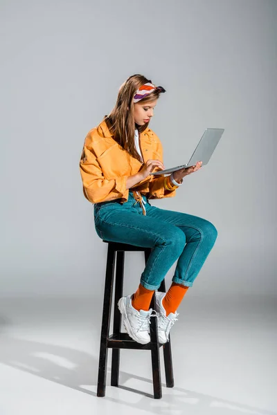 Beautiful blogger using laptop while sitting on stool on grey — Stock Photo