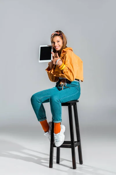 Hermosa chica mostrando el pulgar hacia arriba y la tableta con pantalla en blanco en gris - foto de stock