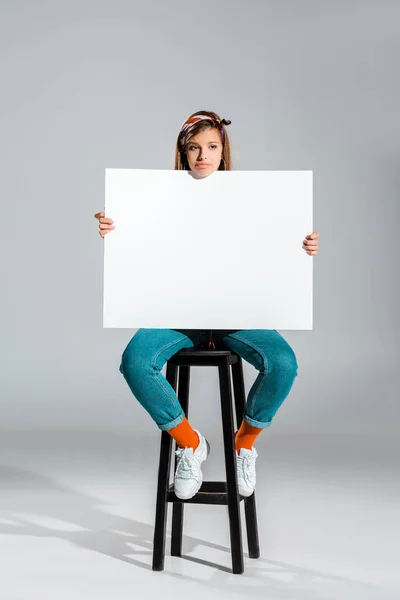 Atractiva chica triste sosteniendo cartel en blanco en gris - foto de stock