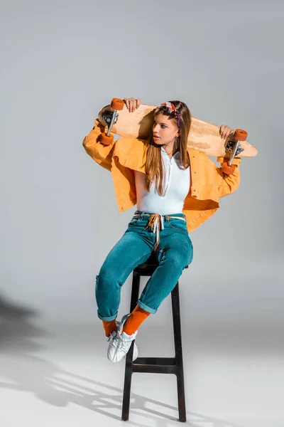 Attrayant élégant fille posant avec longboard sur tabouret sur gris — Photo de stock