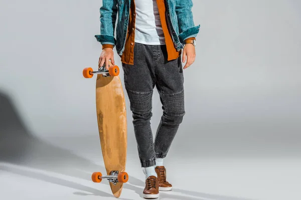 Cropped view of young stylish skateboarder posing with longboard on grey — Stock Photo