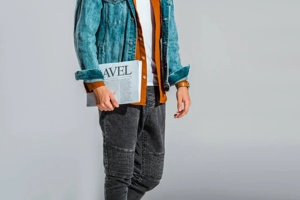 Cropped view of man in denim jacket with travel newspaper isolated on grey — Stock Photo