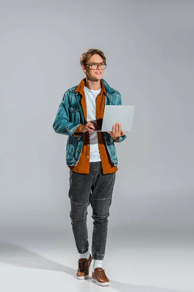 Bel giovane freelance in giacca di denim con computer portatile su grigio — Foto stock