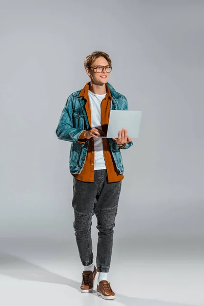 Handsome young freelancer in denim jacket using laptop on grey — Stock Photo