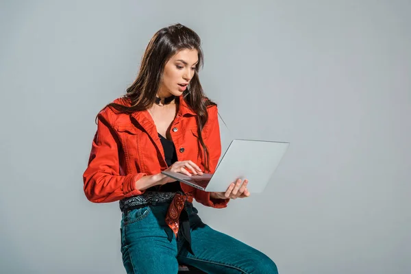 Shocked young woman using laptop isolated on grey — Stock Photo