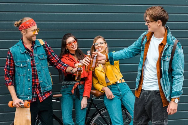 Young smiling friends with bicycle clinking with beer bottles on street — Stock Photo
