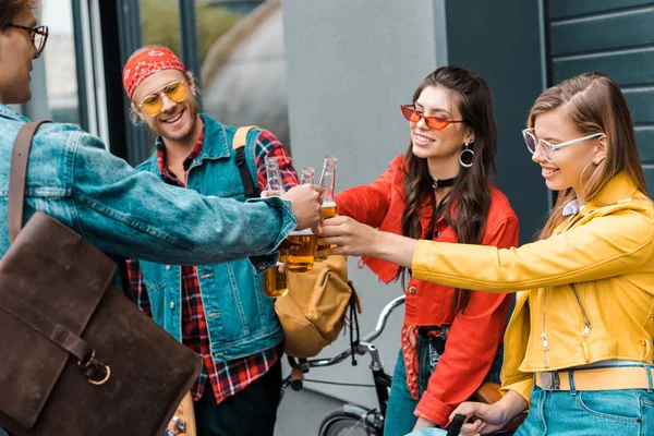 Молодые улыбающиеся друзья с велосипедом звон с бутылками пива на улице — стоковое фото