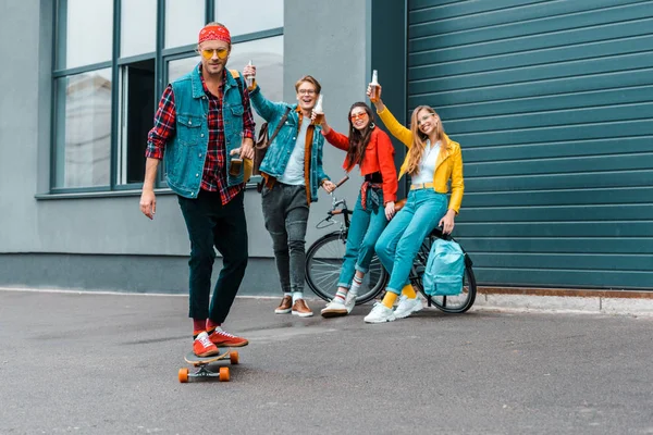 Jovens amigos felizes com skate e bicicleta se divertindo na rua — Fotografia de Stock