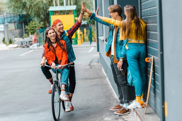 Casal elegante andar de bicicleta e dando highfive aos amigos na rua — Fotografia de Stock