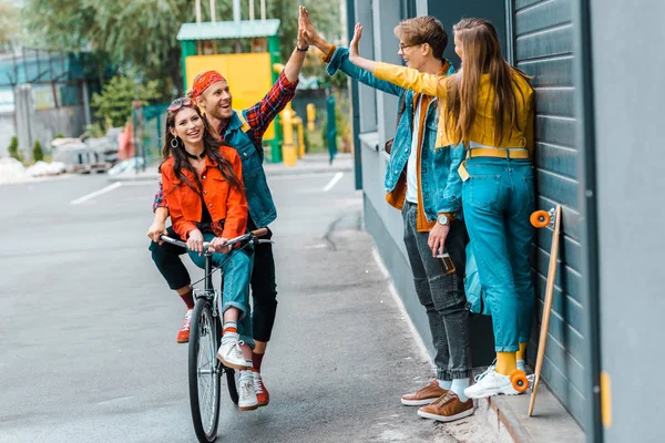 Pareja elegante montar en bicicleta y dar highfive a los amigos en la calle - foto de stock