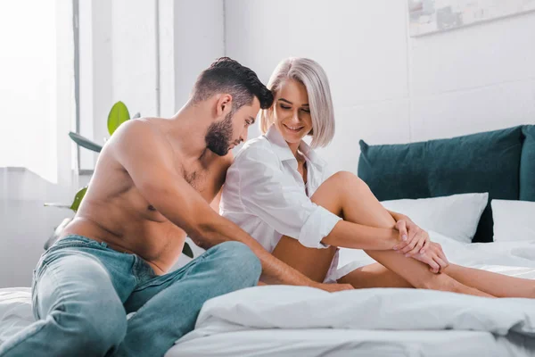 Feliz jovem casal abraçando e sentado na cama juntos — Fotografia de Stock