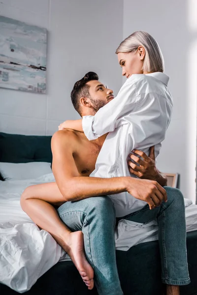 Jovem apaixonado sentado na cama com namorada sedutora no topo — Fotografia de Stock