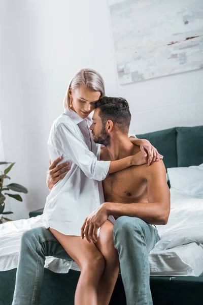 Atractiva pareja joven abrazando mientras se sienta en la cama juntos - foto de stock