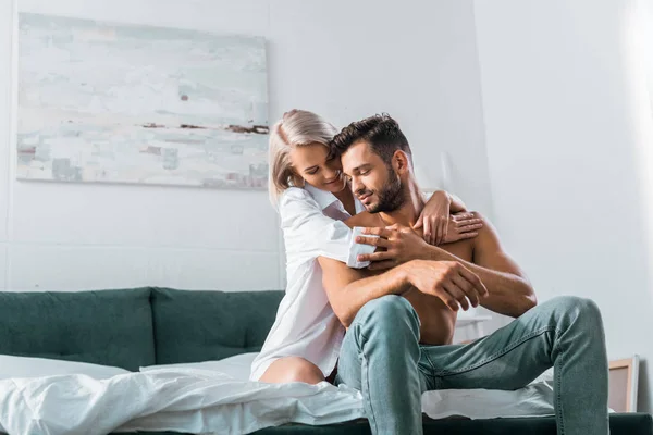 Attractive young woman embracing her boyfriend from behind in bedroom — Stock Photo