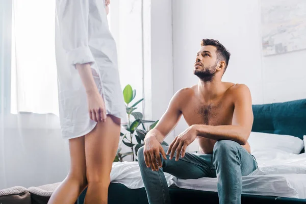 Plan recadré de la femme en chemise debout devant son petit ami alors qu'il est assis sur le lit — Photo de stock