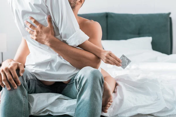 Обрезанный снимок страстной пары с презервативом, сидящей на кровати — стоковое фото