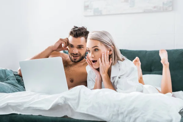 Choqué jeune couple en utilisant ordinateur portable ensemble dans la chambre — Photo de stock