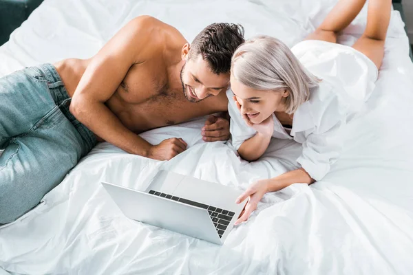 Vista ad alto angolo di felice giovane coppia utilizzando computer portatile insieme in camera da letto — Stock Photo