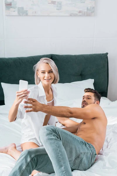 Juguetona joven pareja tomando selfie juntos en dormitorio - foto de stock