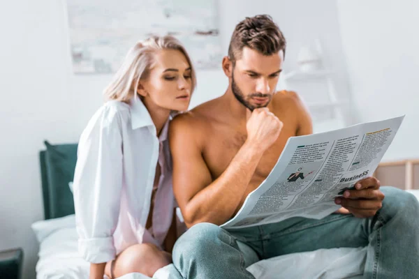 Atractiva pareja joven leyendo el periódico juntos en el dormitorio - foto de stock