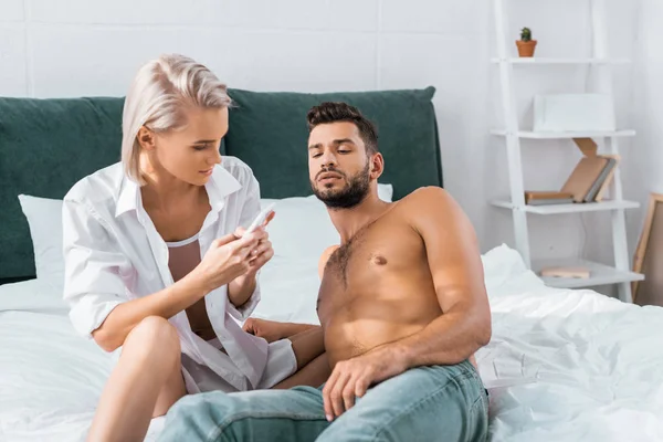 Jealousy young woman using smartphone of her confused boyfriend in bedroom — Stock Photo