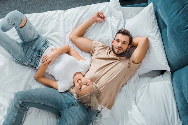 Вид сверху на молодую пару лежащую на кровати в спальне и смотрящую в камеру — стоковое фото