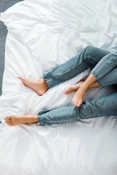 Cropped image of young couple in jeans lying on bed in bedroom — Stock Photo