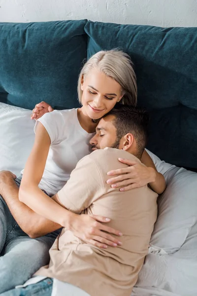 Vista de ángulo alto de feliz pareja joven abrazándose en la cama en el dormitorio - foto de stock