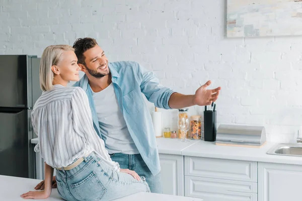 Petit ami souriant montrant quelque chose à petite amie dans la cuisine — Photo de stock