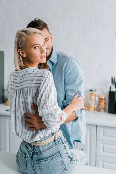 Чуттєва молода пара обіймається на кухні, дівчина дивиться на камеру — стокове фото