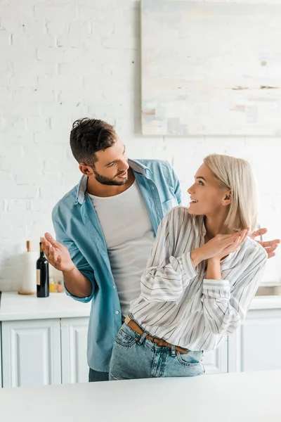 Lächelndes junges Paar schaut einander an und gestikuliert in der Küche — Stockfoto