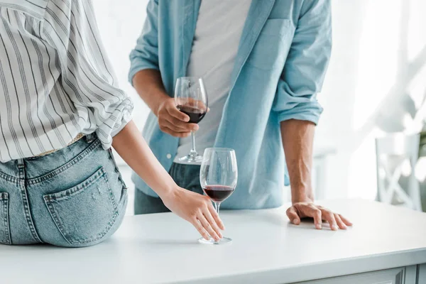 Cropped image of couple with glasses of red wine in kitchen — Stock Photo