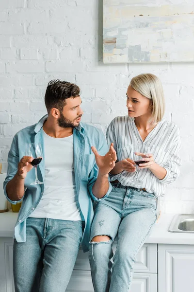 Young couple talking and holding glasses of wine in kitchen — Stock Photo