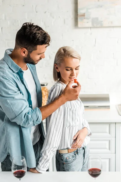 Guapo novio alimentación novia con cereza tomate en cocina - foto de stock