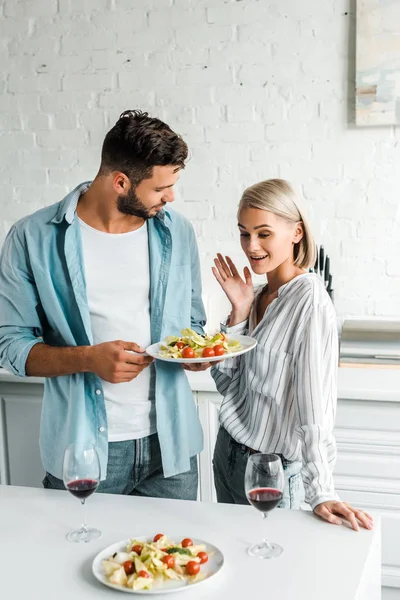 Überraschte Freundin gestikuliert und blickt auf Teller mit Salat in Küche — Stockfoto