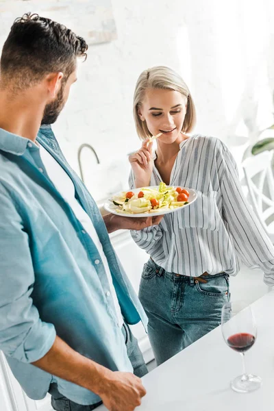 Attraente fidanzata mangiare insalata fresca dal piatto in cucina — Foto stock