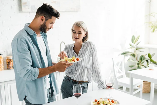Jovem casal comer salada fresca de prato na cozinha — Fotografia de Stock