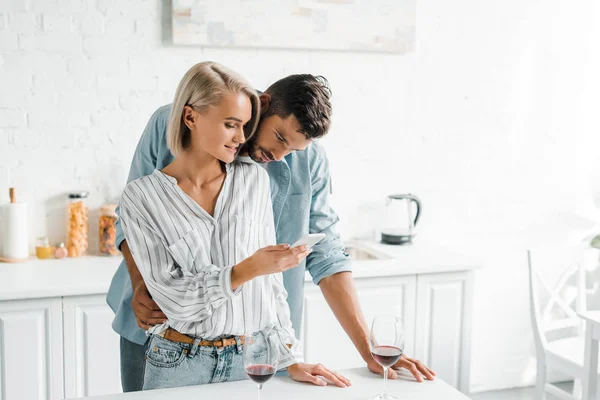 Pareja joven mirando el teléfono inteligente juntos en la cocina - foto de stock