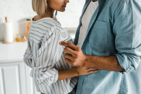 Image recadrée de copain étreignant petite amie et tenant préservatif dans la cuisine — Photo de stock