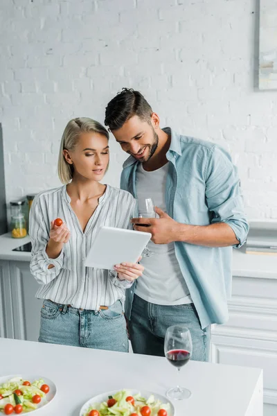 Lächelndes junges Paar schaut in Küche auf Tablet — Stockfoto