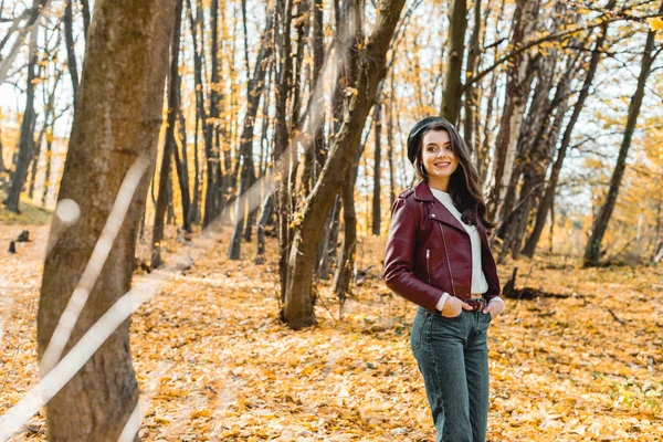 Селективный фокус счастливой стильной девушки в берете, позирующей в желтом осеннем лесу — стоковое фото