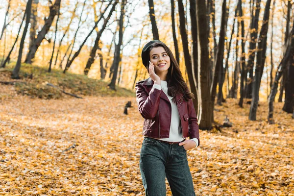 Щаслива модна дівчина в шкіряній куртці розмовляє на смартфоні в автономному лісі — стокове фото