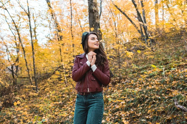 Низкий угол зрения на модную молодую женщину в берете и кожаной куртке, смотрящую в лес — стоковое фото