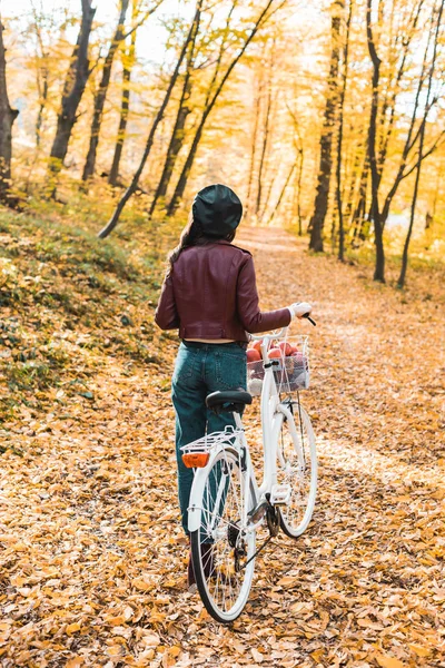 Vista trasera de chica en elegante chaqueta de cuero y boina llevando bicicleta en bosque otoñal amarillo - foto de stock