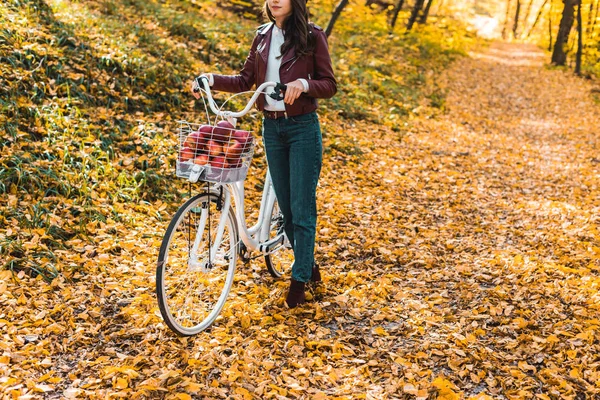 Vista parcial de chica en elegante chaqueta de cuero y boina llevando bicicleta en bosque otoñal amarillo - foto de stock