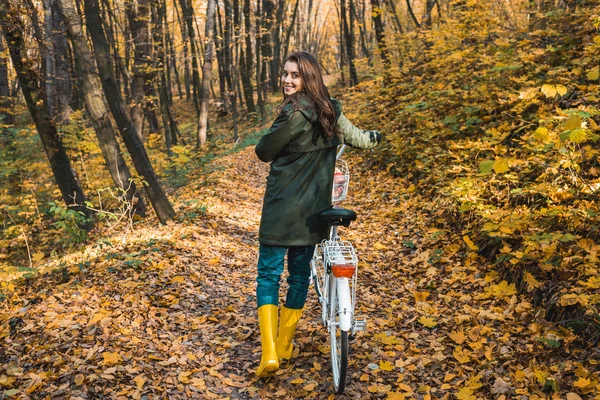 Feliz joven mujer llevando bicicleta en el bosque otoñal amarillo - foto de stock