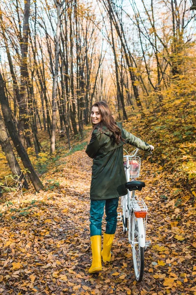 Alegre mujer atractiva llevando bicicleta en bosque otoñal amarillo - foto de stock